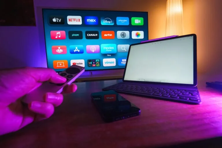 a hand holding a remote pointing to a monitor with apps on it